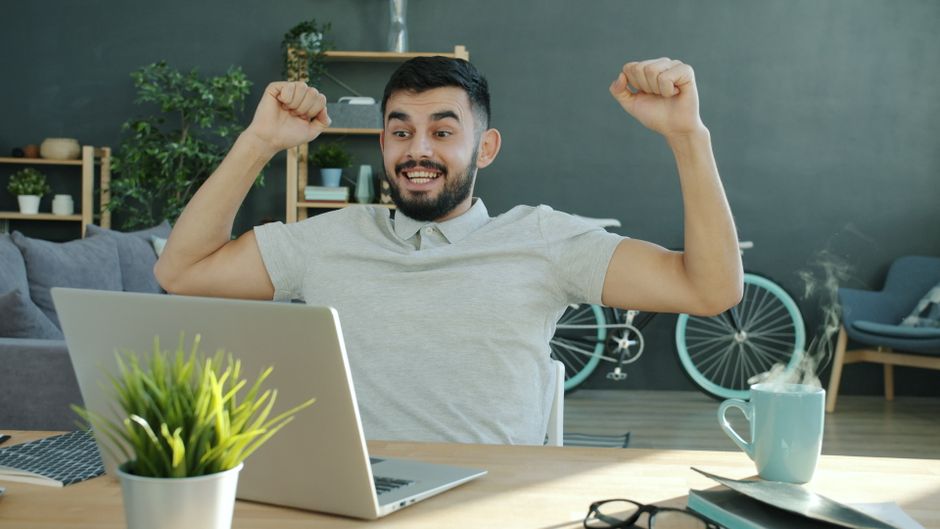 Hombre feliz celebrando éxito mientras trabaja en su laptop en una oficina en casa.