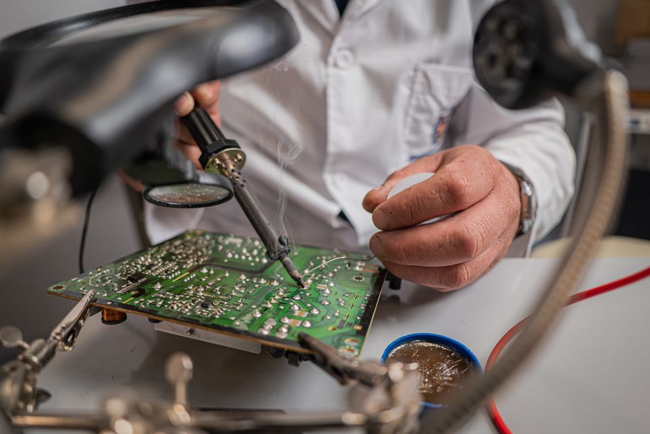 Primer plano de técnico usando un soldador en una placa de circuito en un entorno de laboratorio.