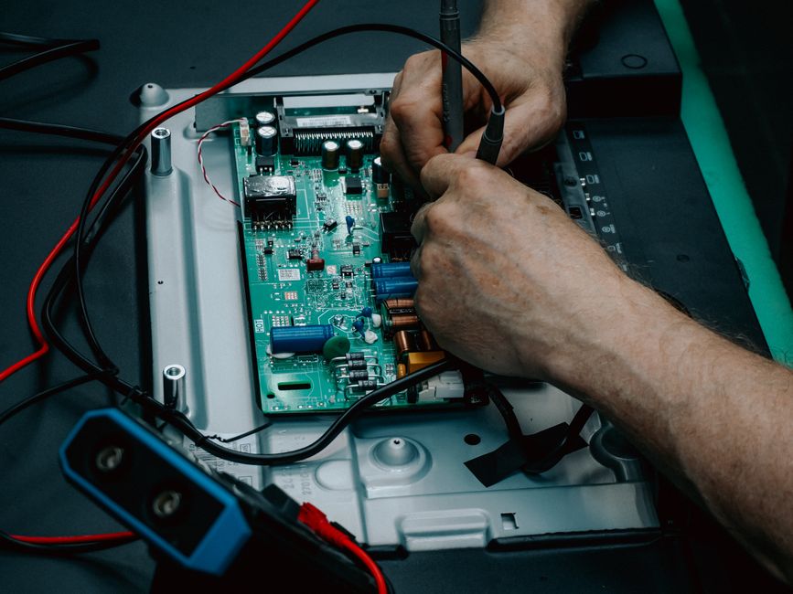 Primer plano de manos reparando una placa de circuito electrónico, mostrando trabajo técnico detallado